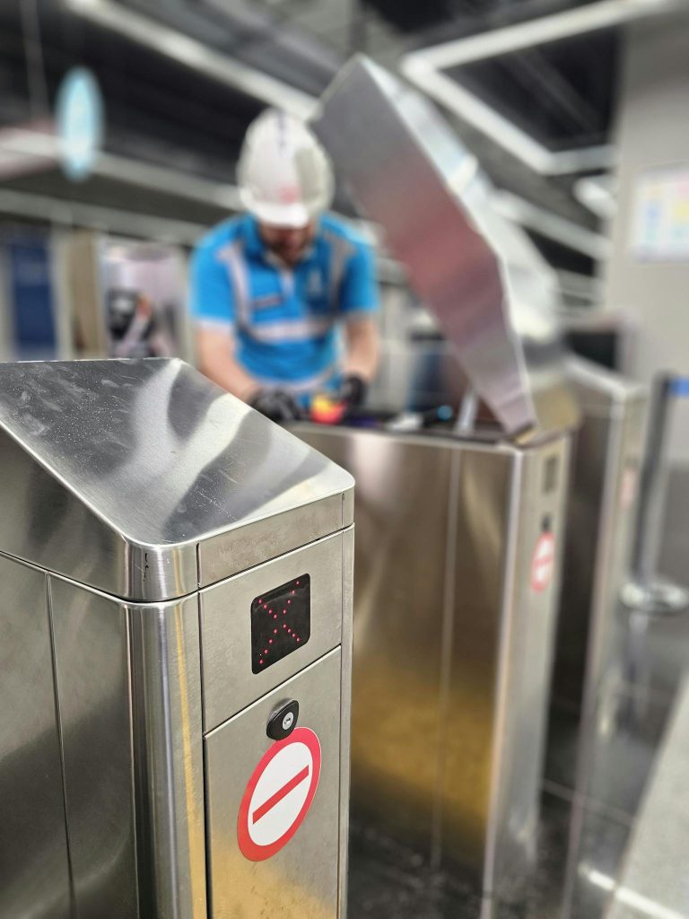 Close-up of a technician repairing a metro station turnstile gate.